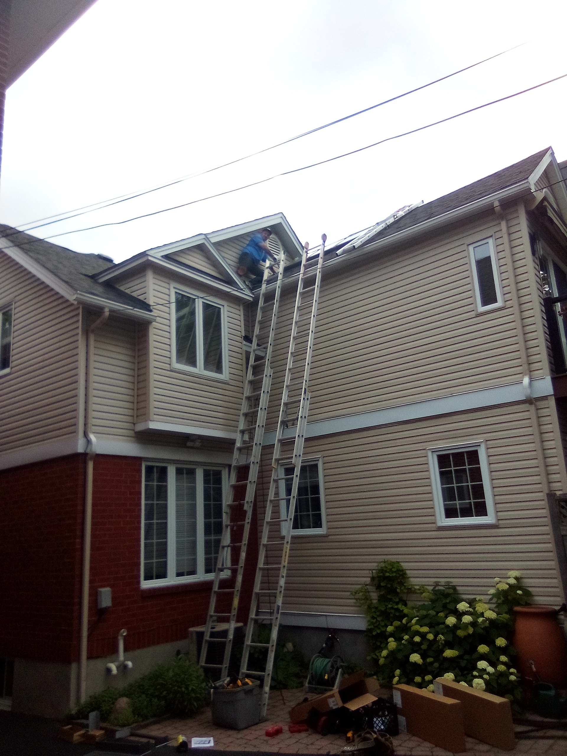 Crew setting up ladders on residential home exterior for skylight installation